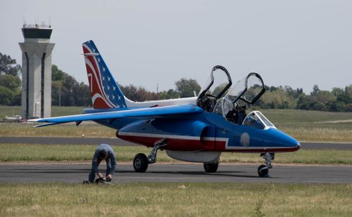 Free Military aircraft with patriotic design, parked on tarmac with technician working nearby. Stock Photo