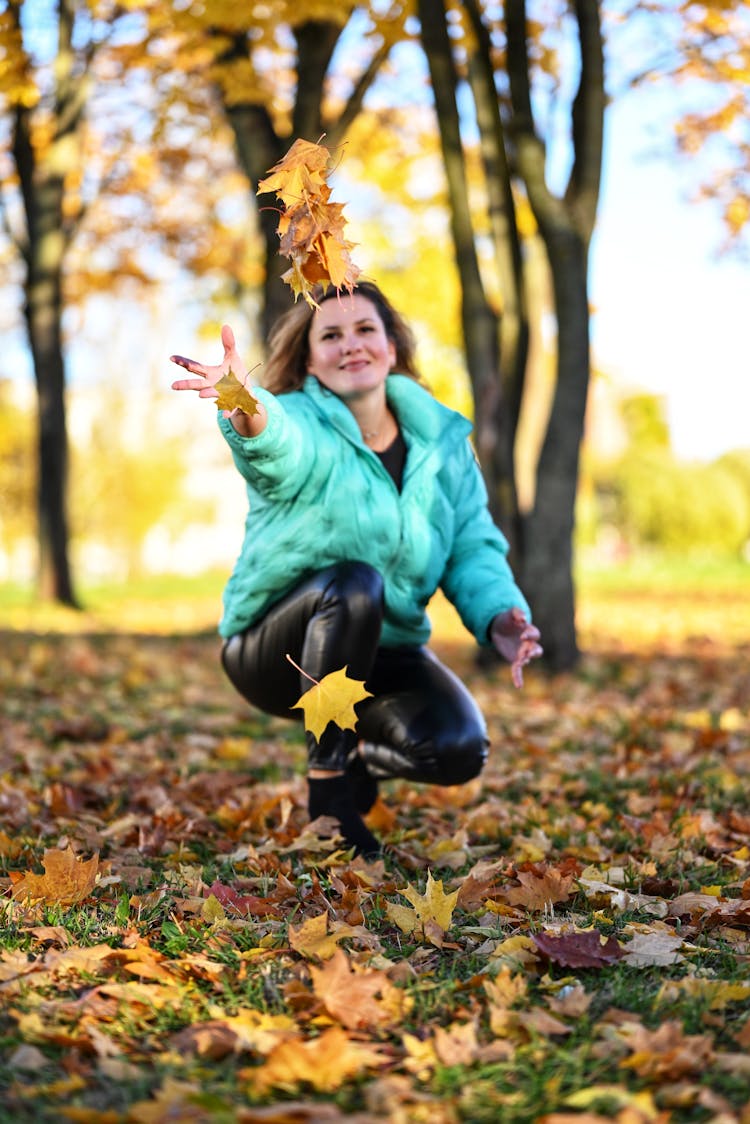 Woman In Green Jacket And Black Leather Pants Throwing Maple Leaves