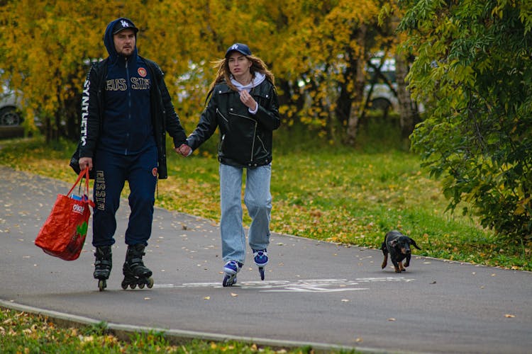 Couple Rollerskating In A Park With Their Dog 