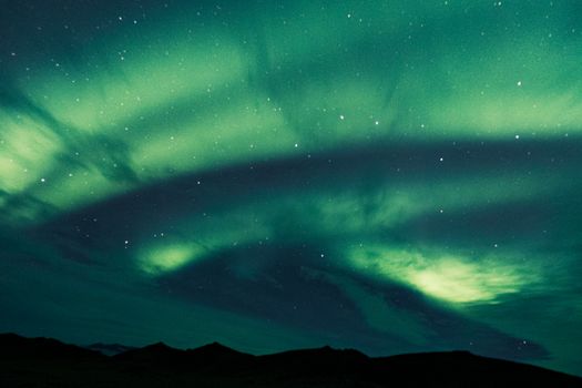Stunning view of aurora borealis illuminating the night sky over a silhouette of mountains.