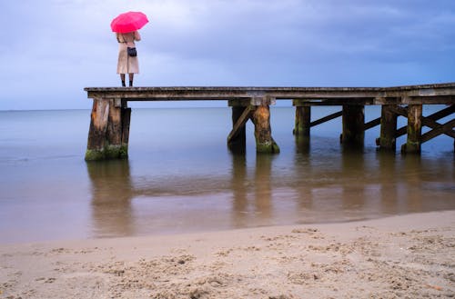 Person with a Pink Umbrella Standing on a Wooden Dock