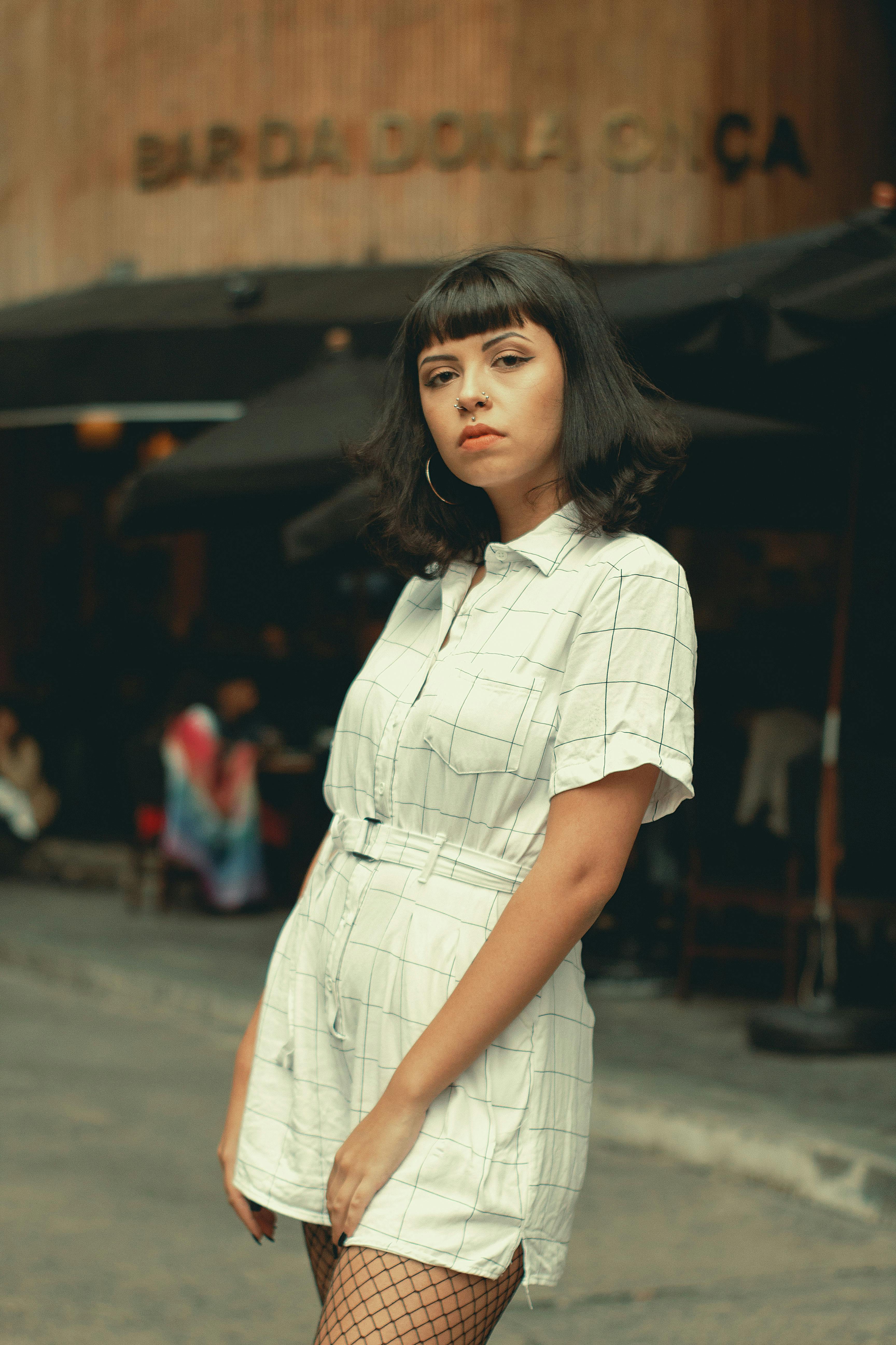 Young woman in white playsuit with fringe and fishnets posing on São Paulo street.