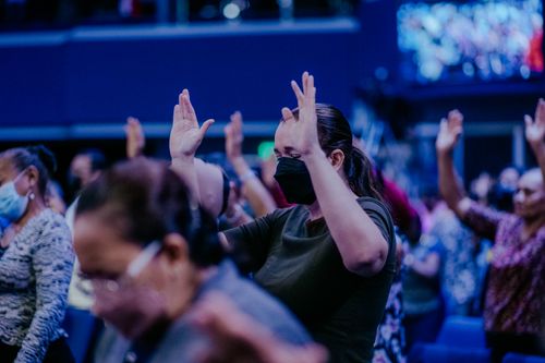 Free Women worship indoors with raised hands and face masks, capturing vibrant religious fervor. Stock Photo