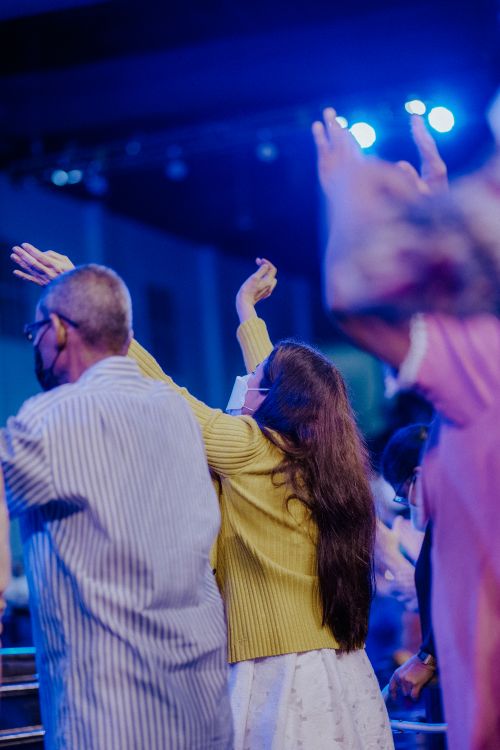 Free People raising arms in excitement at a lively indoor concert with blue stage lights. Stock Photo