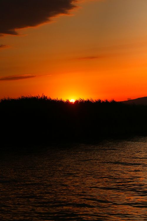 Free A stunning sunset casting silhouettes over a body of water, capturing the serene beauty of nature. Stock Photo