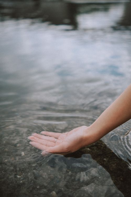 Free Close-up of a woman's hand gently touching a clear water surface outdoors, creating ripples. Stock Photo