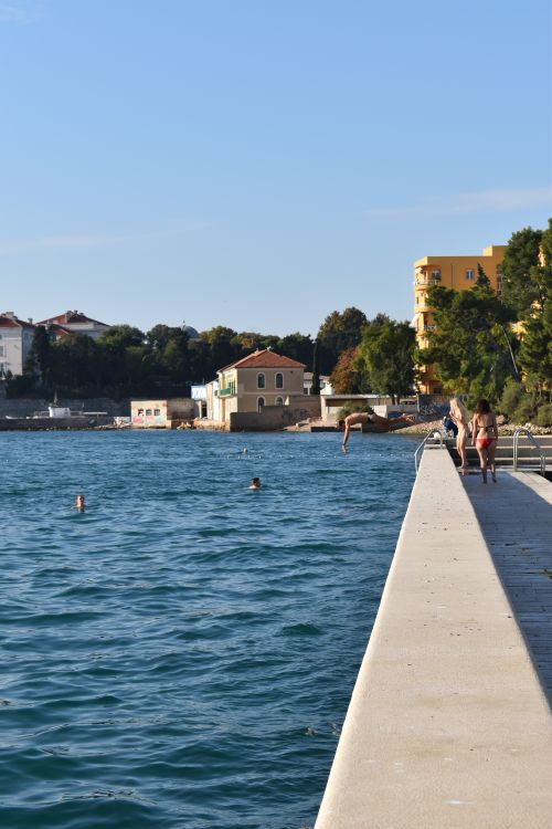 Free People enjoying a sunny day at a coastal town harbor with clear skies and vibrant waters. Stock Photo