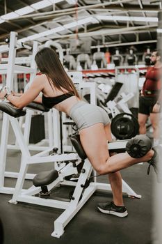 Woman performing leg exercise on a gym machine, wearing sportswear.