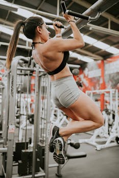 Athletic woman doing pull-ups in a gym, showcasing strength and determination.
