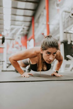 A determined woman doing push-ups in a modern gym with fitness equipment in the background.