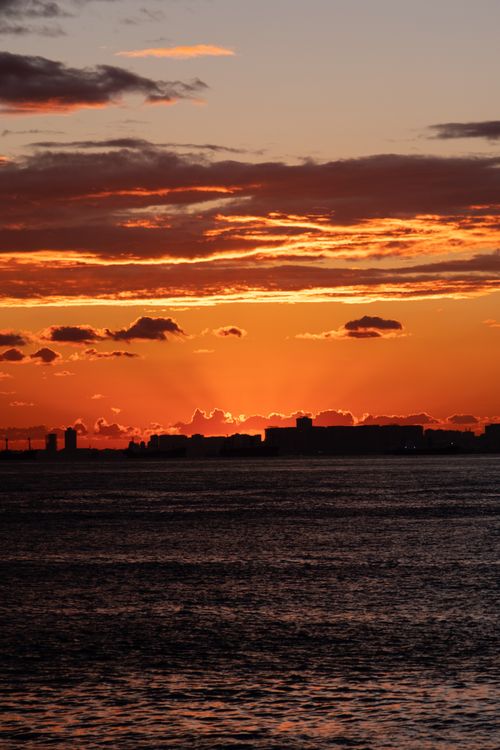 Free Silhouette of city skyline at sunset with vivid orange sky reflecting over calm water. Stock Photo