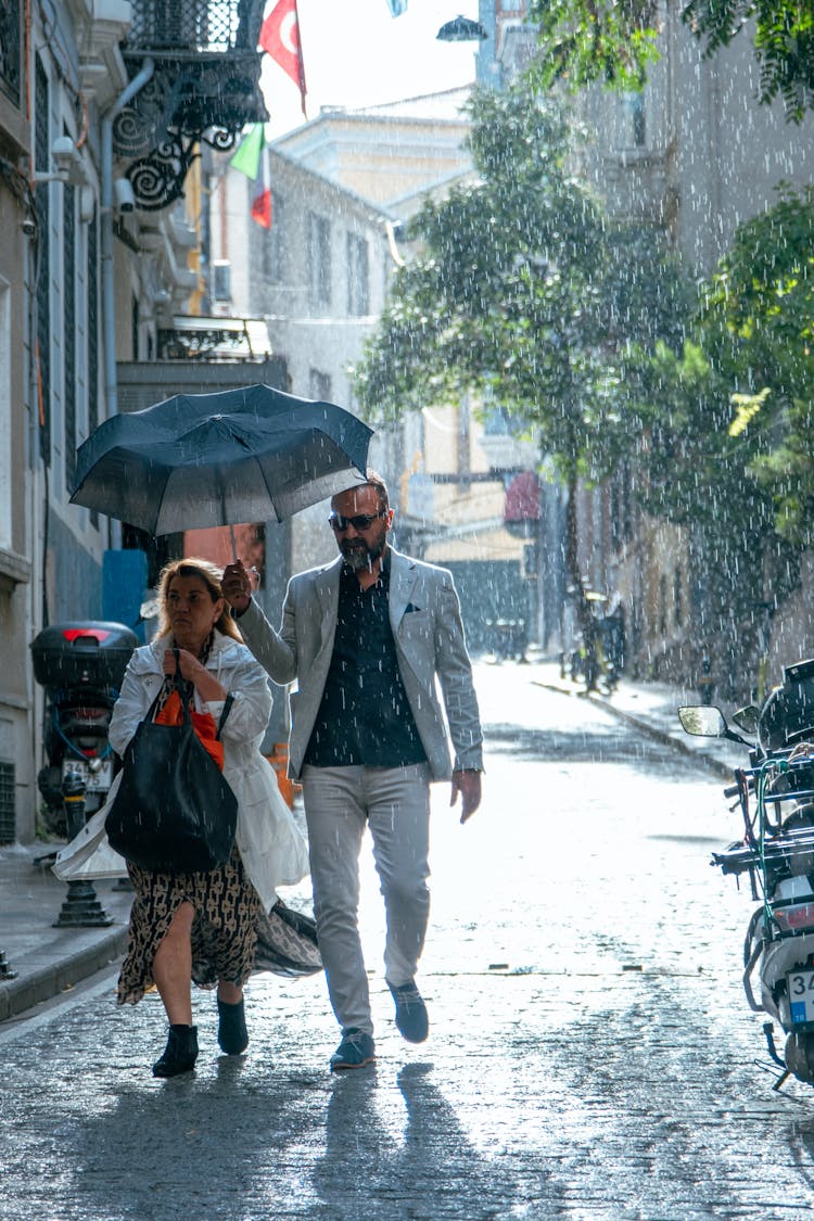 Man And Woman Walking Under An Umbrella In A Rain On An Old Town Street