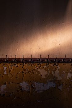 Wall with peeling paint and rusty hooks illuminated by soft light, showcasing texture and decay.