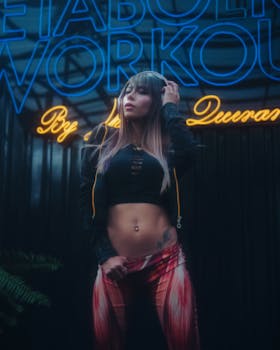 Fashionable woman stands confidently with headphones by a neon-lit workout sign.