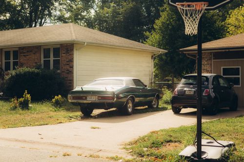 Free A serene suburban driveway featuring a classic car and a basketball hoop under a clear sky. Stock Photo
