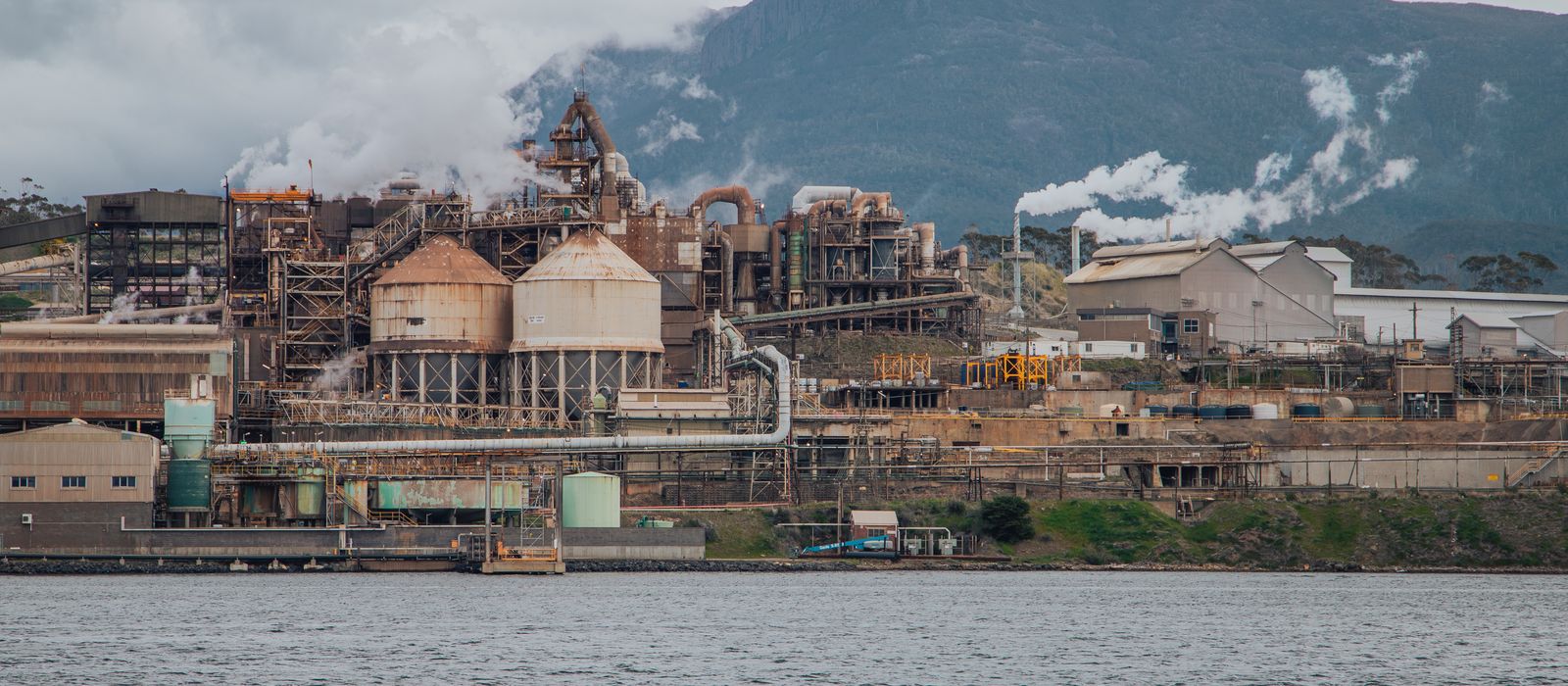 View of an industrial refinery against Mount Wellington in Hobart, Australia, by a river.