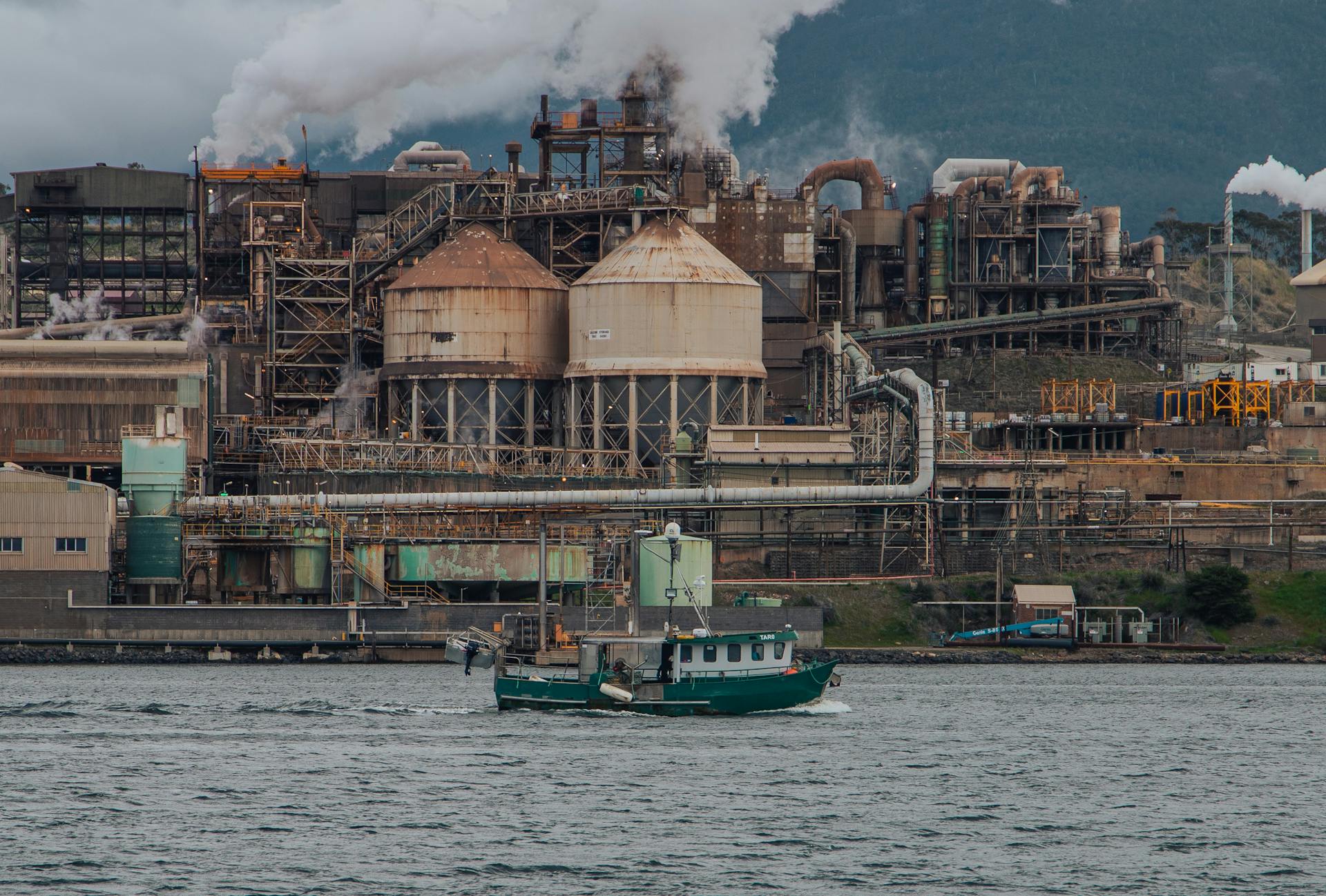 A cargo ship sails past an industrial area in Hobart, showcasing industry and water transportation.