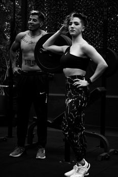 Two adults posing confidently in a gym setting with fitness equipment.