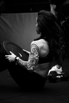 Athletic woman with tattoos exercises indoors holding a weight plate in black and white.