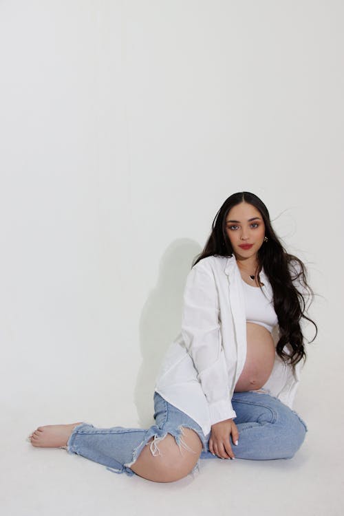 Pregnant Woman on White Long Sleeves and Ripped Jeans Sitting on Floor 