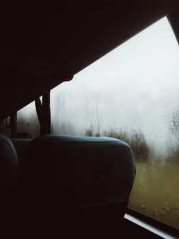 View from inside a bus with raindrops on window, capturing a moody and introspective atmosphere.