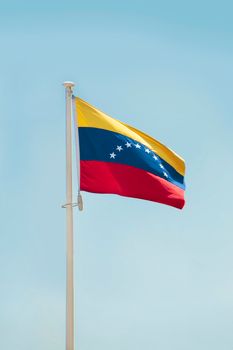 A vibrant Venezuelan flag waves proudly on a flagpole against a clear blue sky.