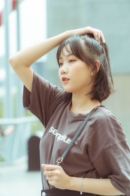 Stylish young woman posing casually, with hand on hair, standing outdoors in a sunny setting.