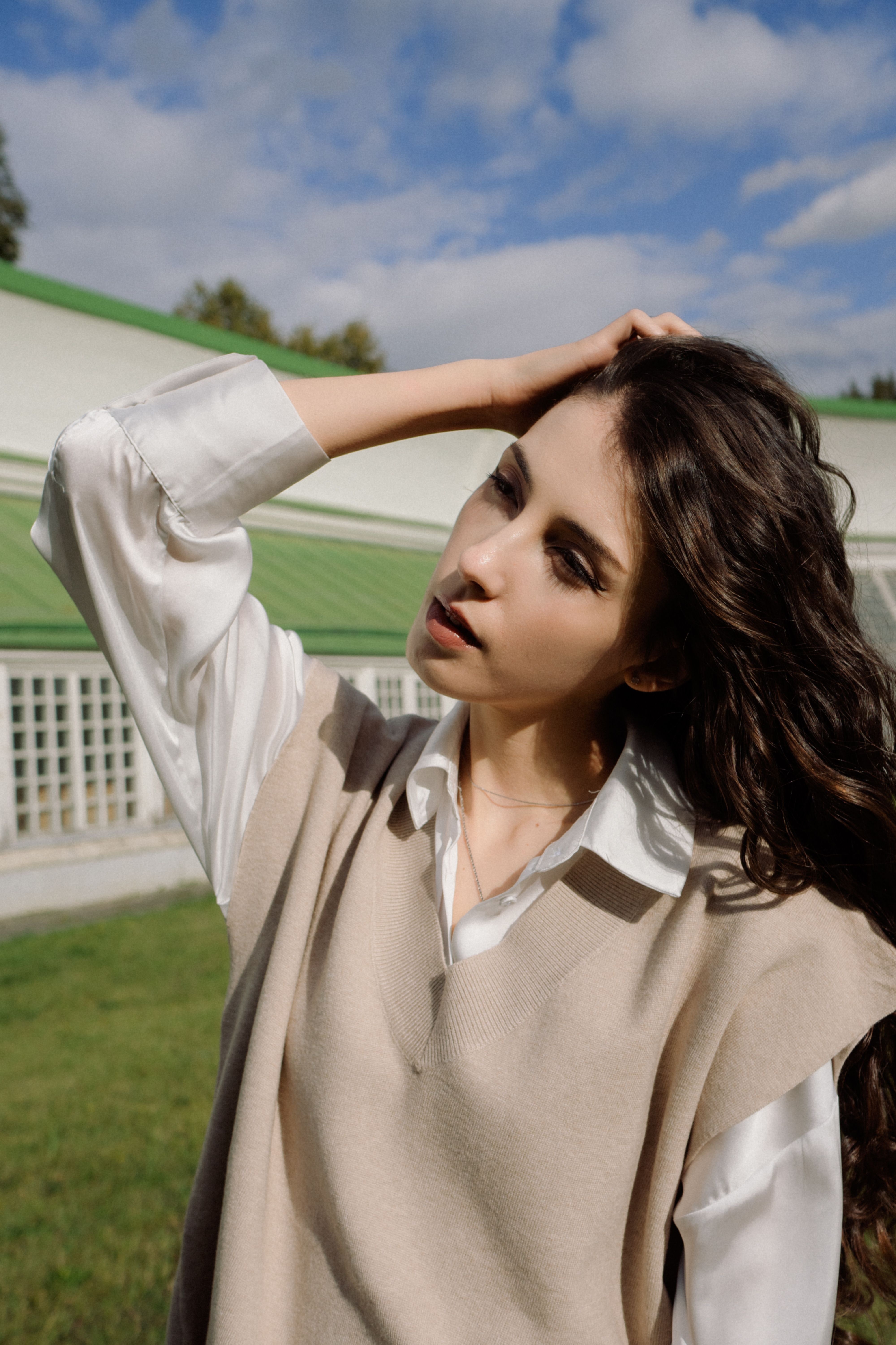 Elegant portrait of a woman in a vest and blouse, posing outdoors on a sunny day.