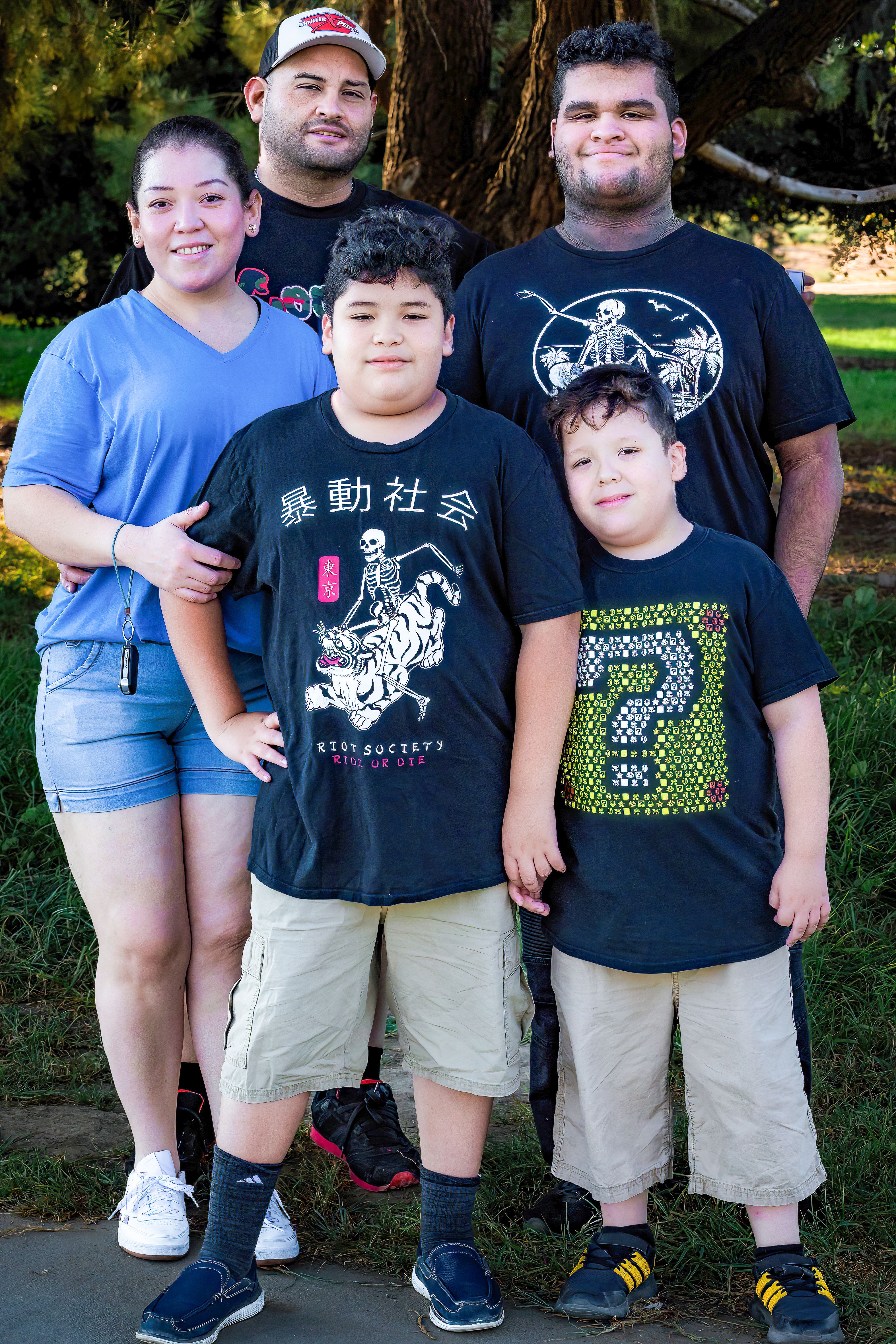 Family of five posing together outdoors, casual attire, happy expressions.