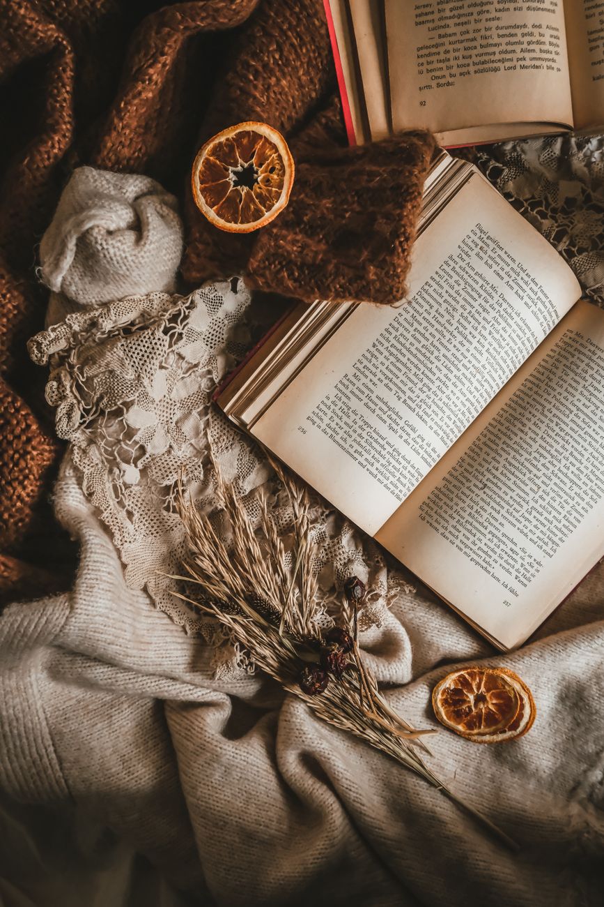 Warm and cozy still life featuring an open book, dried oranges, and textured fabric in soft lighting.