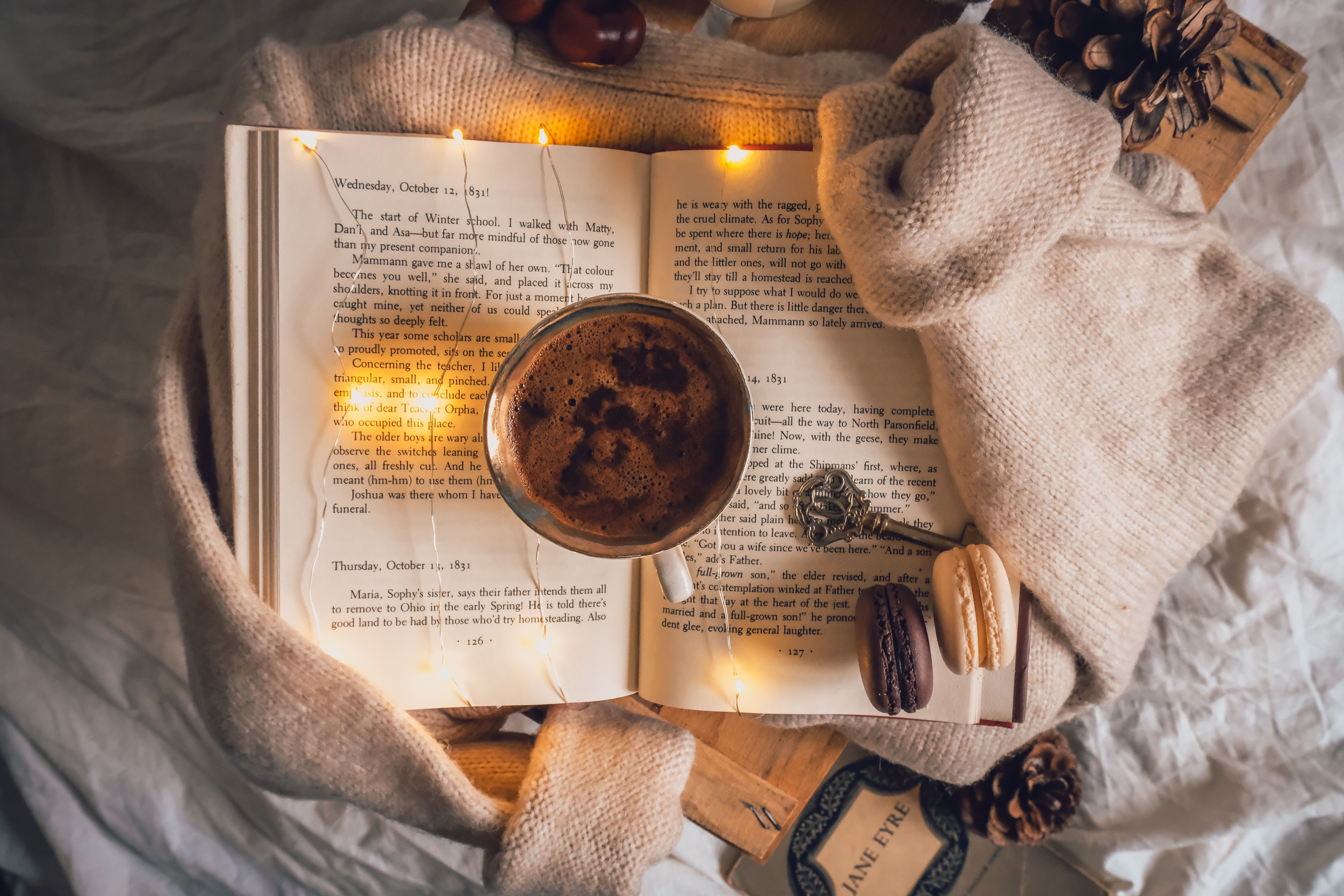 Warm and cozy setup with coffee, open book, sweater, and macarons for a relaxing autumn day.