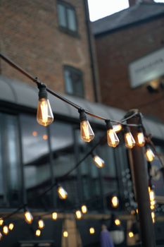 String of vintage-style light bulbs hanging outside a brick building in a city setting.
