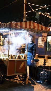 Atmospheric night scene of a street vendor selling corn in Istanbul with vibrant streetcar in background.