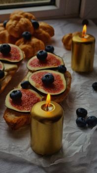 Cozy breakfast setting with figs, blueberries, and lit candles creating a warm atmosphere.