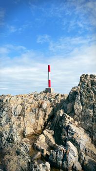 A striking red marker pole atop rocky terrain under a clear blue sky in a natural setting.