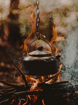 Close-up of a metal kettle hanging over a campfire in a rustic outdoor setting