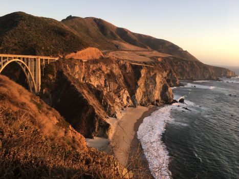 Dramatic sunset view of Bixby Creek Bridge and rugged California coastline along Pacific Ocean.