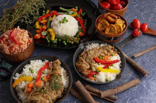A vibrant display of traditional rice dishes with vegetables, plantains, and chicken in iron pans.