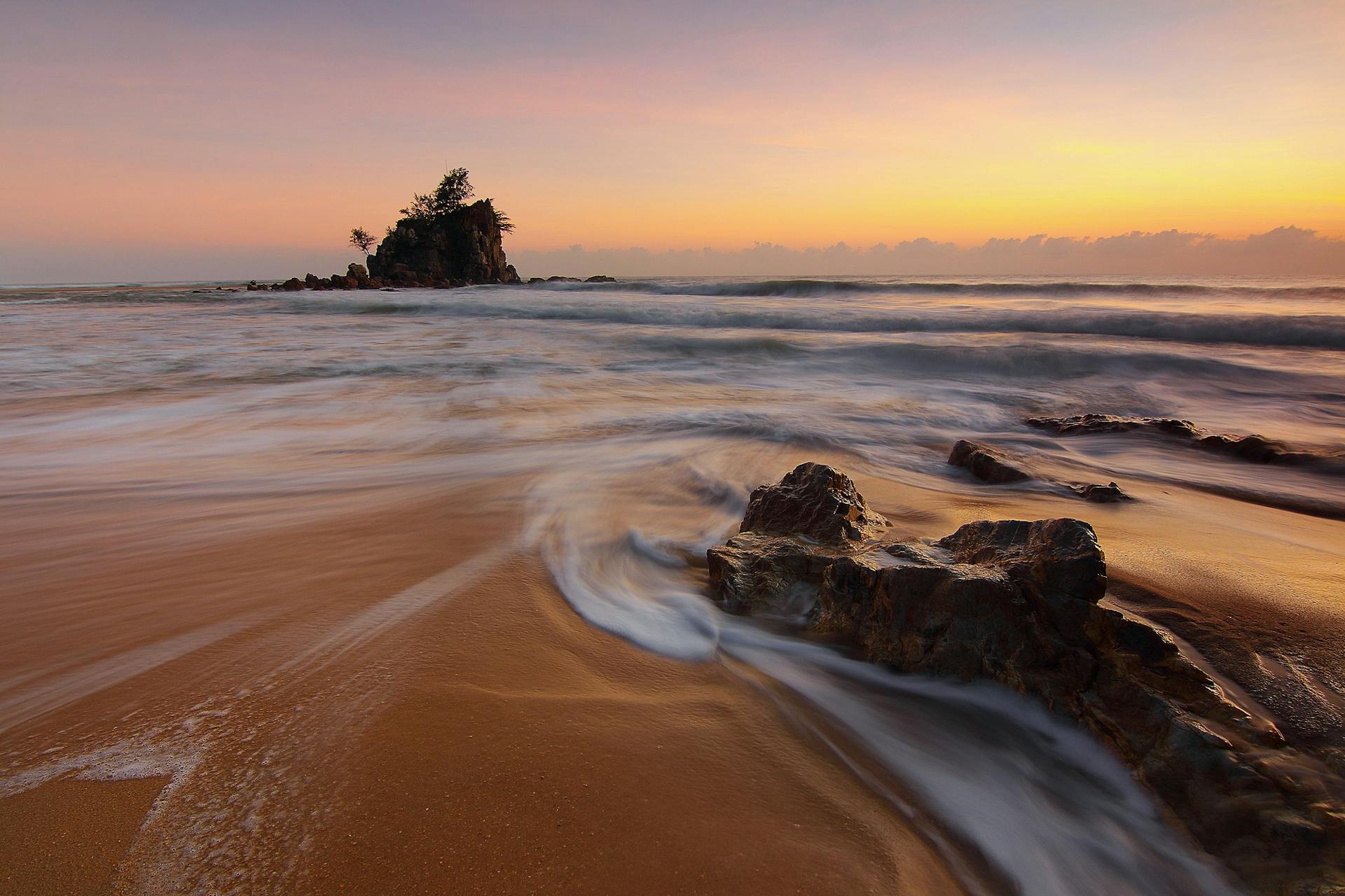 Peaceful beach scene with waves crashing on rocks at sunrise, capturing the beauty of nature.