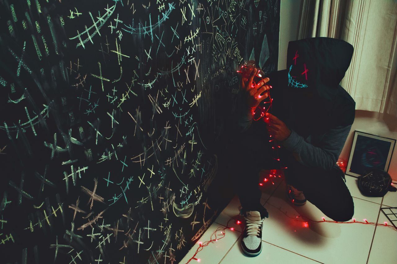 hooded figure with glowing mask crouches in a dimly lit indoor setting