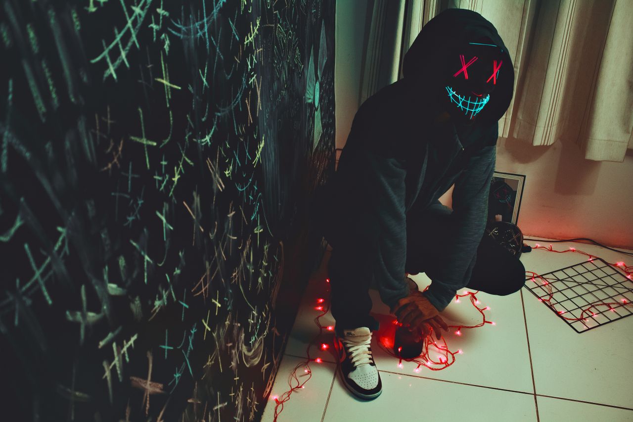 a mysterious figure in a mask glows with neon lights indoors creating