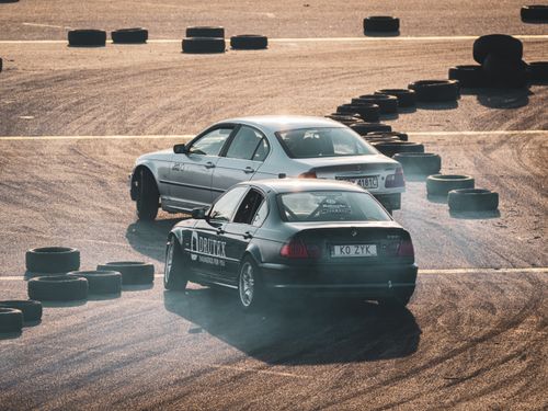Free Two cars skillfully drifting around tire markers on a sunlit race track, capturing thrilling motorsport action. Stock Photo