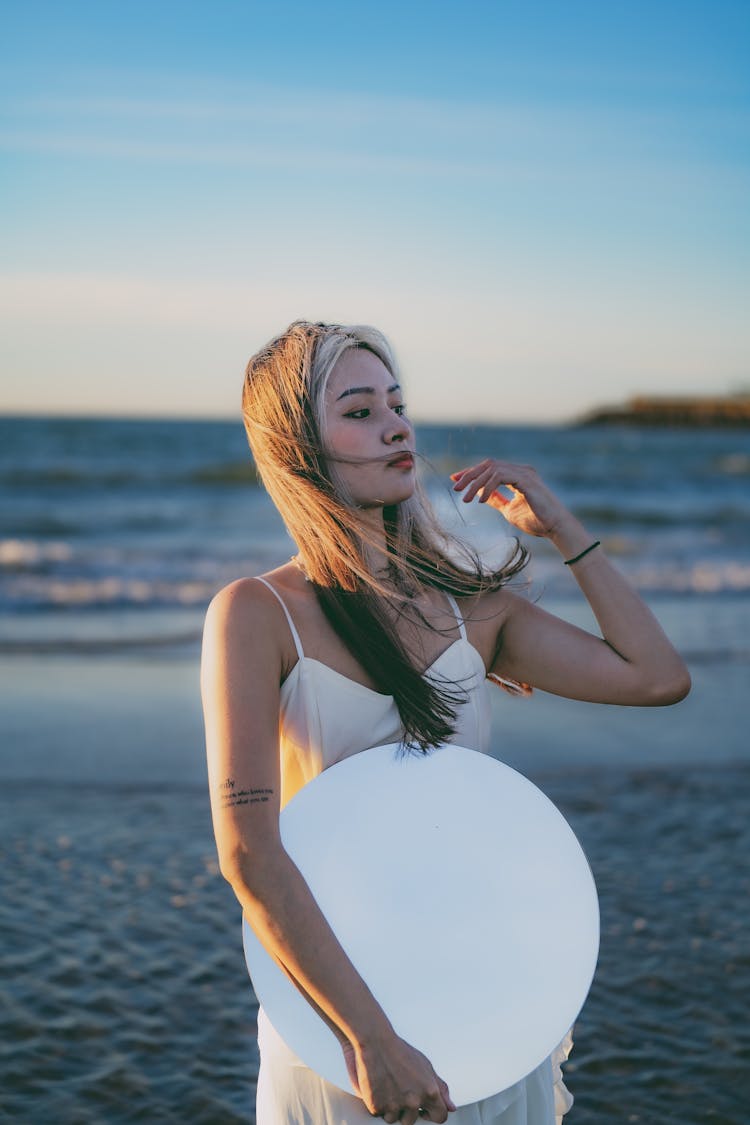 A Woman In A White Dress Holding A Mirror 