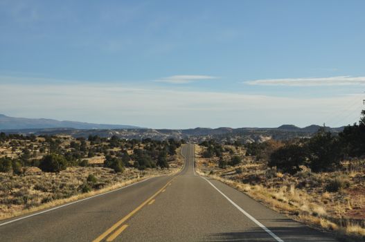 Endless road stretching through arid desert with mountains in the distance under a clear sky.