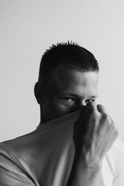 Free A striking black and white portrait of a man partly hiding his face with a shirt. Stock Photo