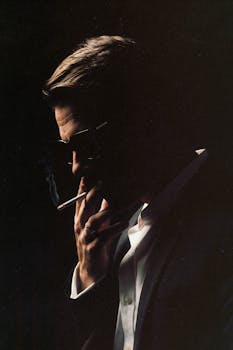 Dramatic silhouette of a man in sunglasses smoking, set against a dark background.