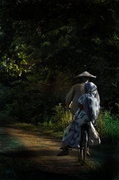 一男一女穿着传统服装，沿着森林小路骑着自行车