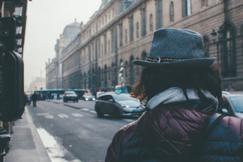 Person Wearing Fedora Hat Walking on Street Near Vehicles