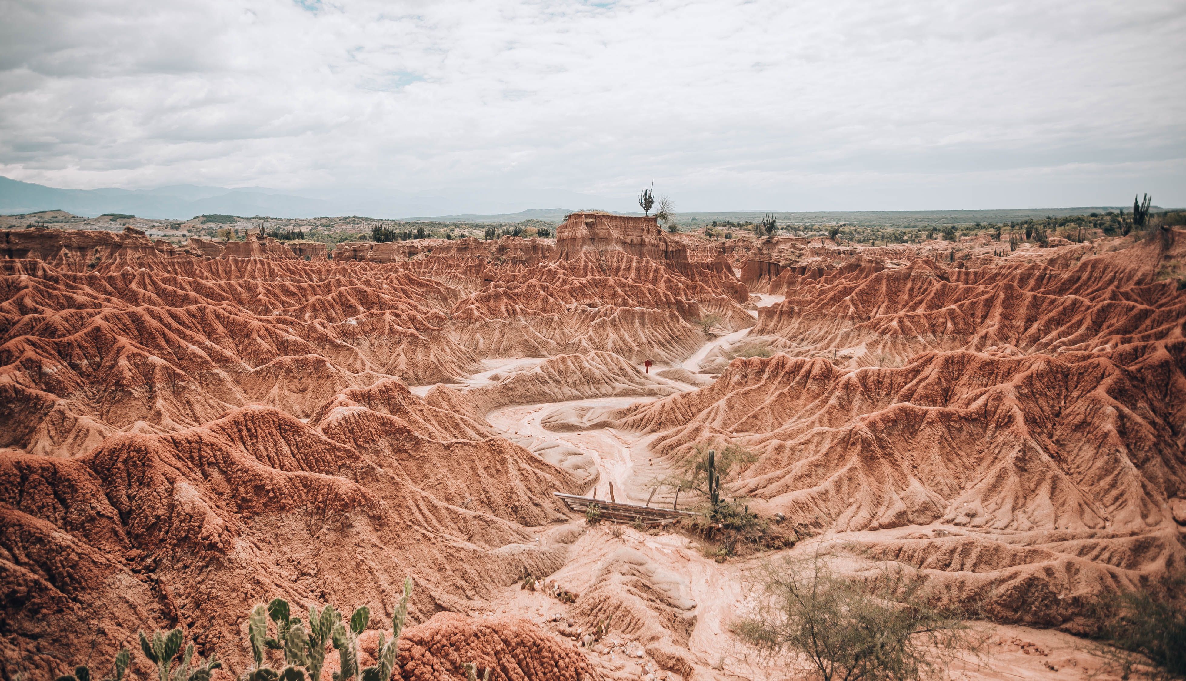 Explore the breathtaking aerial perspective of dramatic red desert landscapes under a cloudy sky. - Desierto de la Tatacoa