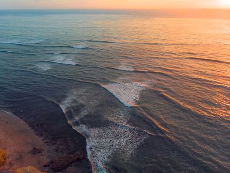Captivating aerial view of ocean waves as they meet the shore during a vibrant sunset.